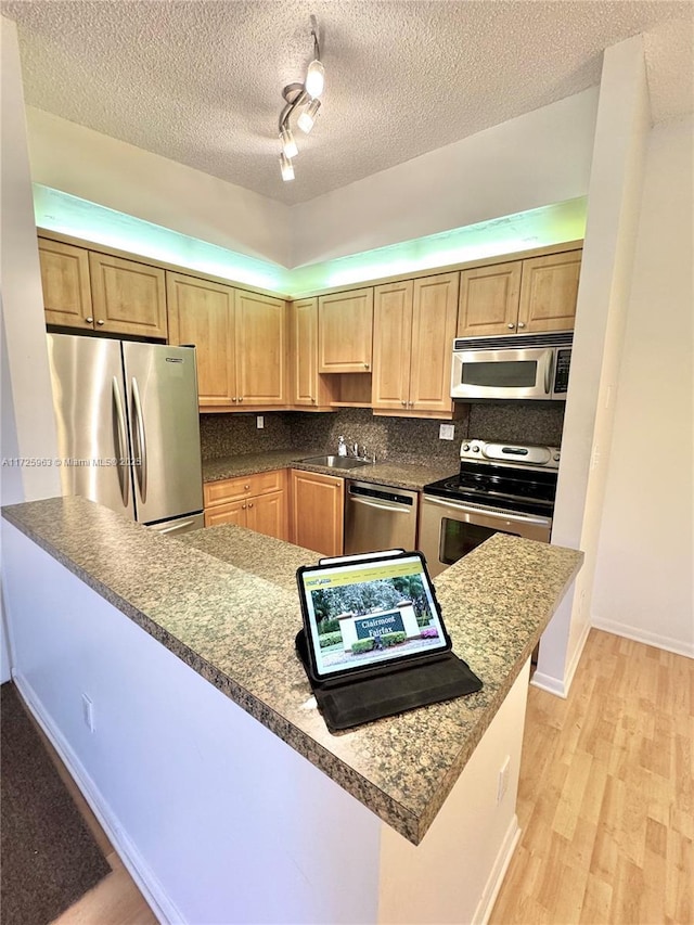 kitchen with sink, appliances with stainless steel finishes, tasteful backsplash, kitchen peninsula, and light wood-type flooring