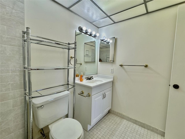 bathroom featuring vanity, a drop ceiling, tile patterned floors, and toilet