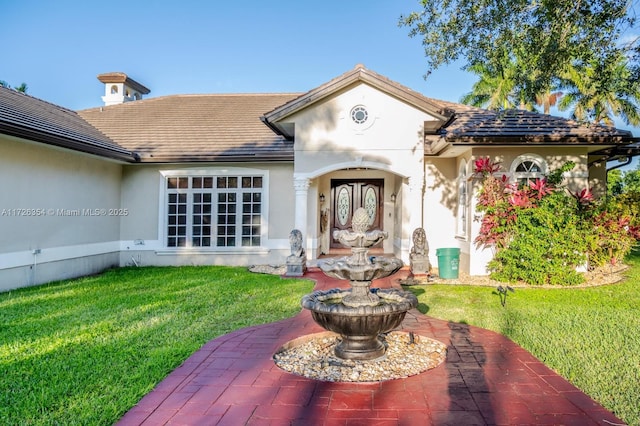 back of property with a tile roof, a yard, and stucco siding