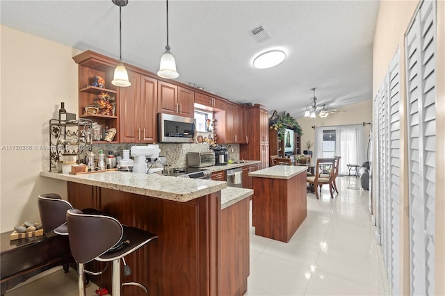 kitchen with decorative light fixtures, ceiling fan, kitchen peninsula, stainless steel appliances, and light tile patterned floors