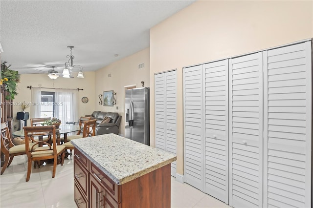 kitchen with a kitchen island, light tile patterned flooring, hanging light fixtures, a textured ceiling, and stainless steel fridge