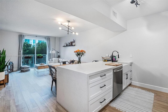 kitchen featuring light countertops, light wood-type flooring, a peninsula, white cabinets, and stainless steel dishwasher