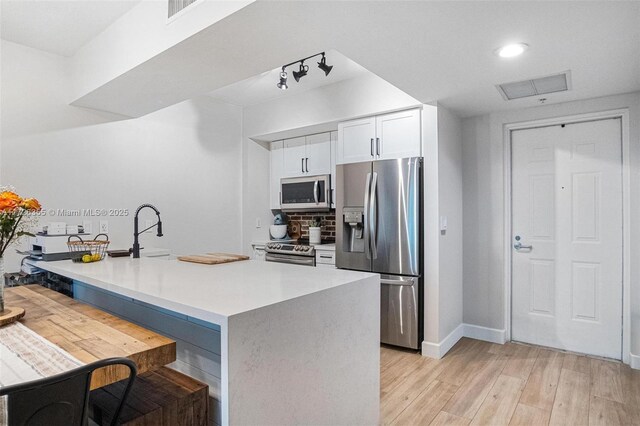 kitchen with white cabinets, light wood-type flooring, and appliances with stainless steel finishes