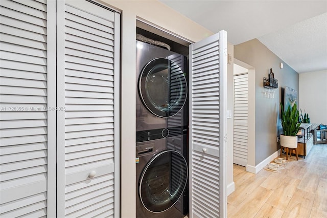 laundry room with stacked washing maching and dryer, a textured ceiling, and light hardwood / wood-style floors