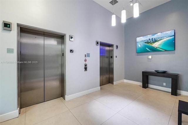 corridor featuring elevator, light tile patterned floors, and baseboards