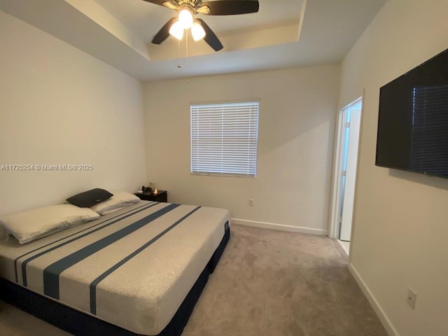 bedroom with a raised ceiling, light colored carpet, and ceiling fan