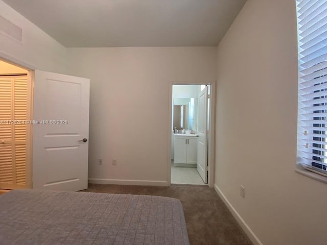 unfurnished bedroom with sink, ensuite bathroom, dark carpet, and a closet