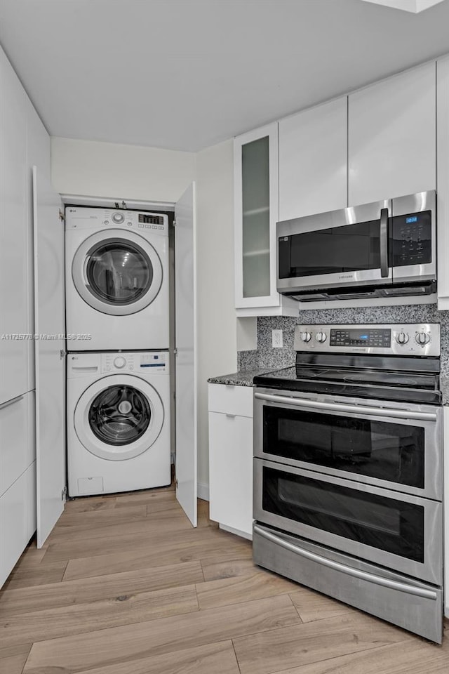 kitchen with light wood-style flooring, white cabinets, stacked washer and clothes dryer, appliances with stainless steel finishes, and backsplash