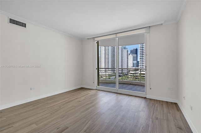 empty room featuring visible vents, a city view, expansive windows, ornamental molding, and wood finished floors