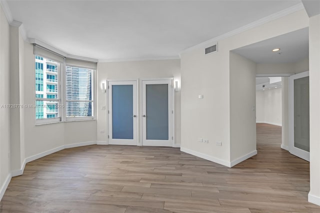 empty room with visible vents, crown molding, baseboards, french doors, and light wood-style floors