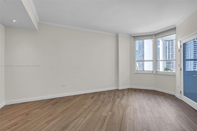 empty room with light wood-type flooring, baseboards, and crown molding