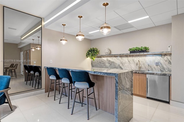 kitchen with light tile patterned floors, refrigerator, a breakfast bar, and a sink