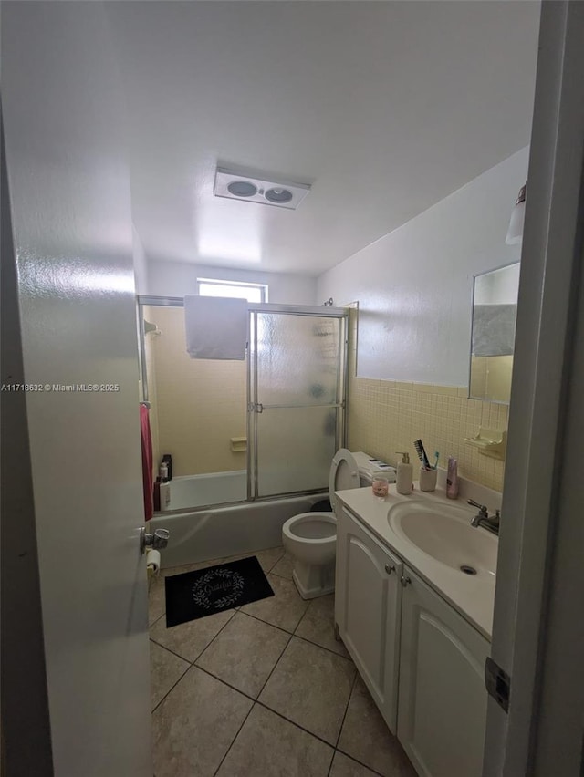 full bathroom featuring toilet, vanity, tile patterned floors, tile walls, and bath / shower combo with glass door