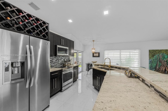 kitchen featuring vaulted ceiling, appliances with stainless steel finishes, light stone counters, decorative light fixtures, and backsplash