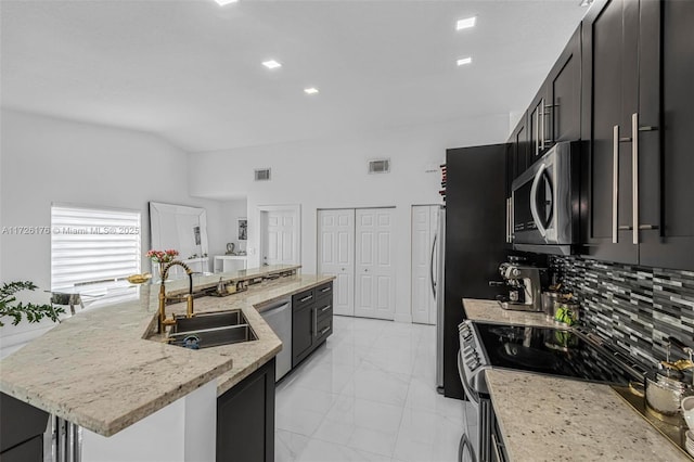 kitchen featuring sink, light stone counters, an island with sink, decorative backsplash, and appliances with stainless steel finishes