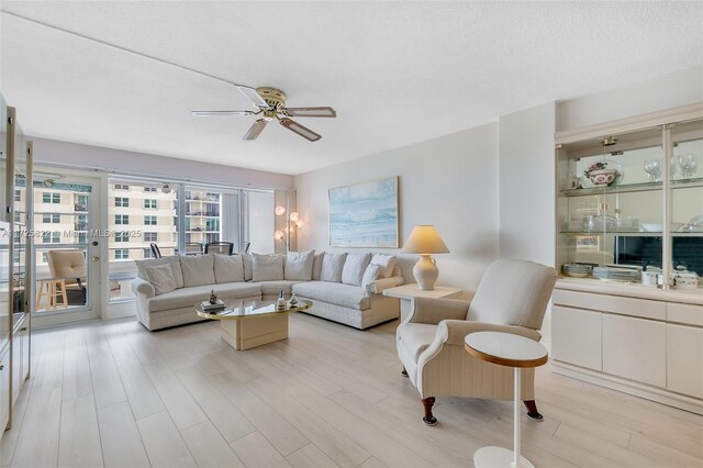 living room with a textured ceiling, ceiling fan, and light hardwood / wood-style flooring