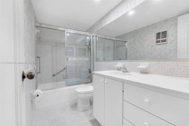 full bathroom with toilet, vanity, tile patterned floors, bath / shower combo with glass door, and backsplash