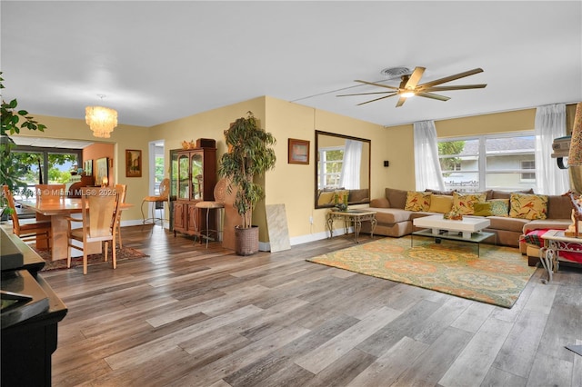 living room featuring ceiling fan with notable chandelier and light wood-type flooring