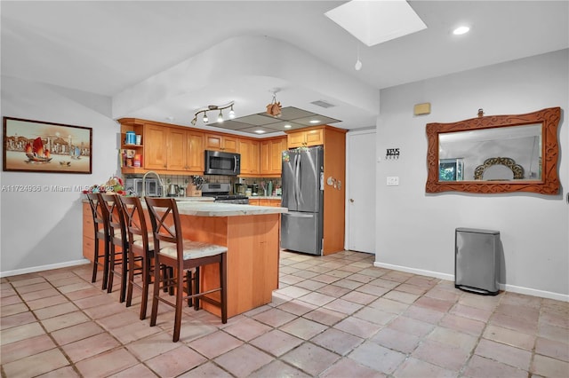 kitchen featuring a kitchen breakfast bar, appliances with stainless steel finishes, a skylight, kitchen peninsula, and tasteful backsplash