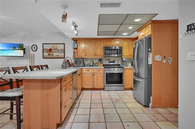 kitchen featuring appliances with stainless steel finishes, kitchen peninsula, a breakfast bar, sink, and tasteful backsplash