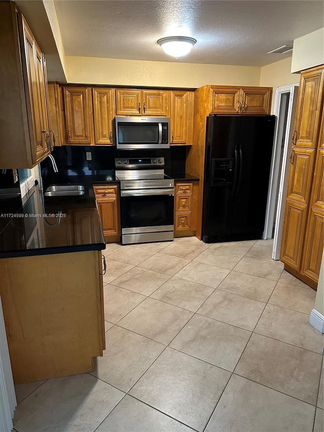 kitchen featuring sink, a textured ceiling, appliances with stainless steel finishes, and light tile patterned flooring