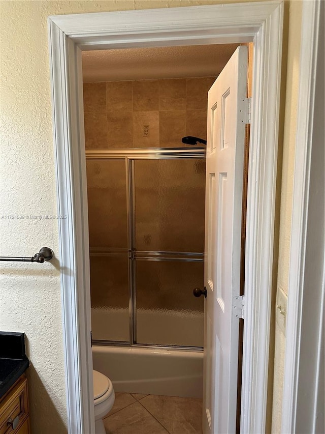 full bathroom with tile patterned floors, bath / shower combo with glass door, toilet, and vanity