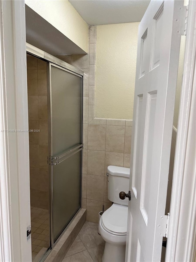 bathroom with toilet, tile walls, tile patterned floors, and walk in shower