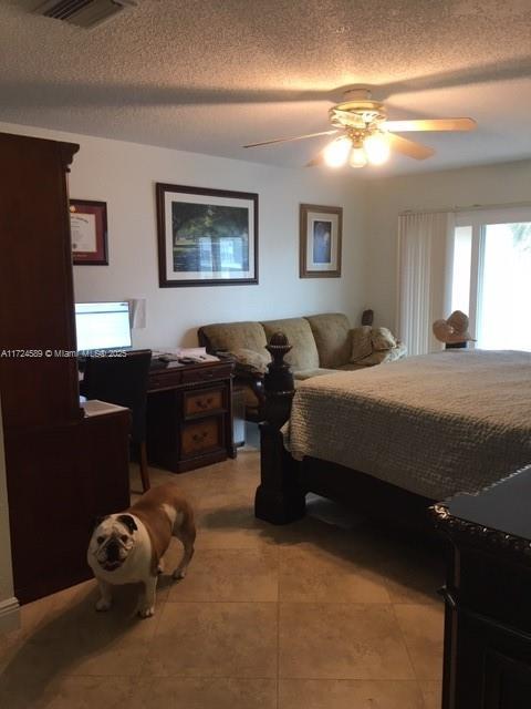 tiled bedroom with ceiling fan and a textured ceiling