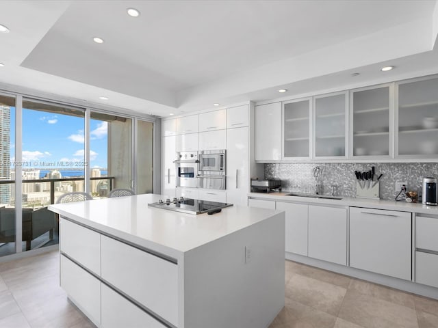 kitchen featuring a kitchen island, a tray ceiling, white cabinets, appliances with stainless steel finishes, and sink