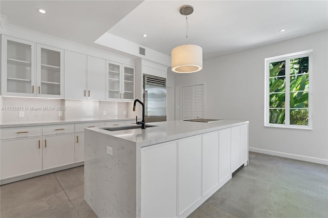 kitchen featuring built in fridge, pendant lighting, an island with sink, white cabinetry, and sink