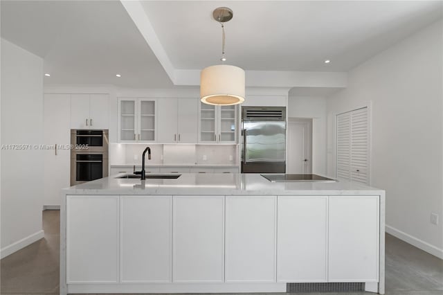 kitchen featuring sink, decorative light fixtures, appliances with stainless steel finishes, an island with sink, and white cabinets