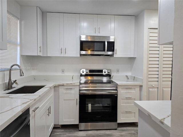 kitchen with white cabinets, stainless steel appliances, light stone counters, and sink