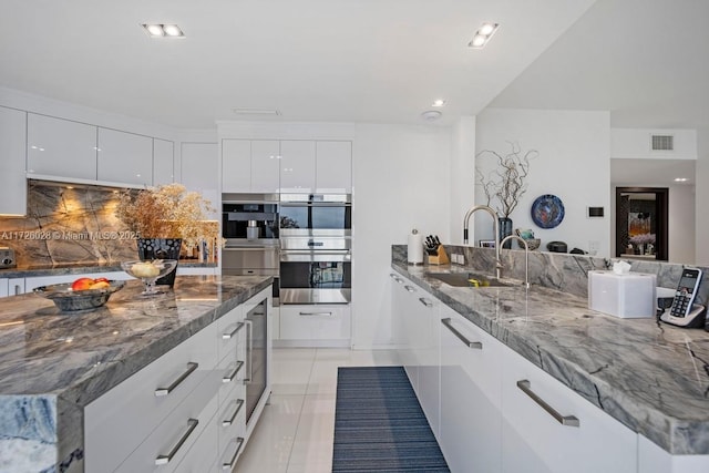 kitchen featuring double oven, a sink, visible vents, and white cabinets