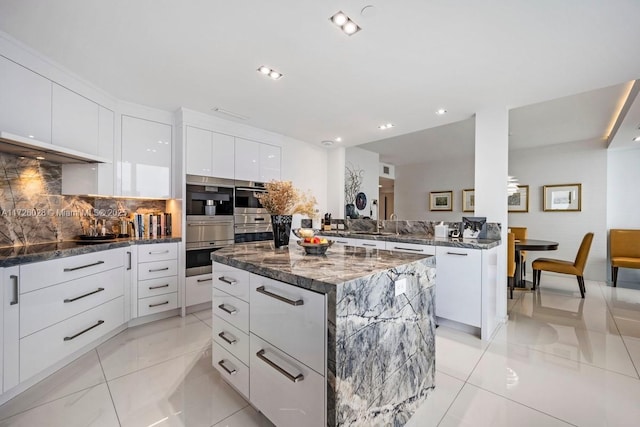 kitchen featuring stainless steel double oven, white cabinets, a kitchen island, light tile patterned flooring, and dark stone countertops