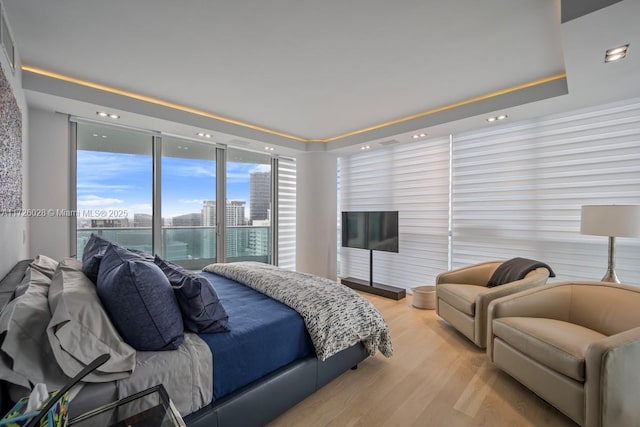 bedroom with light wood-type flooring, a view of city, and a raised ceiling