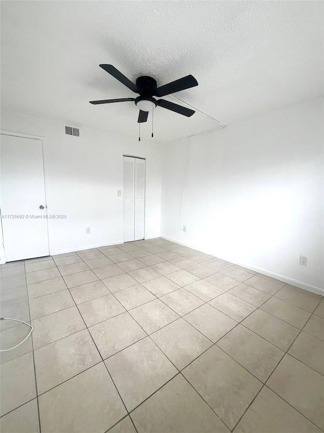 empty room with ceiling fan, a textured ceiling, and light tile patterned floors