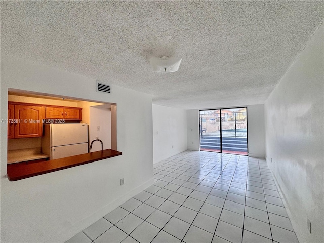 spare room featuring visible vents, baseboards, light tile patterned flooring, and a textured ceiling