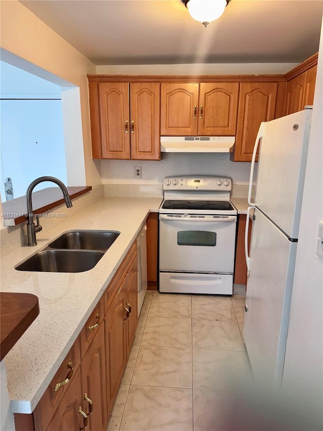 kitchen featuring white appliances, under cabinet range hood, light stone counters, a sink, and brown cabinets