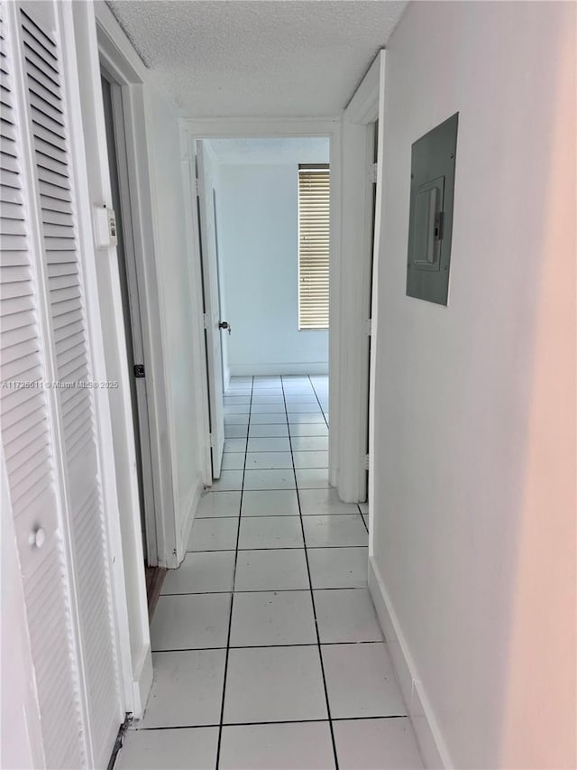 hall featuring light tile patterned floors, baseboards, electric panel, and a textured ceiling