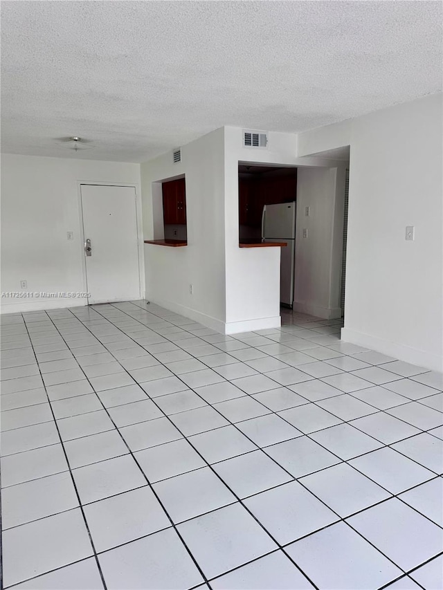 unfurnished living room with a textured ceiling, light tile patterned flooring, and visible vents