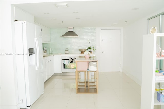 kitchen featuring white appliances, wall chimney range hood, backsplash, white cabinetry, and light tile patterned flooring