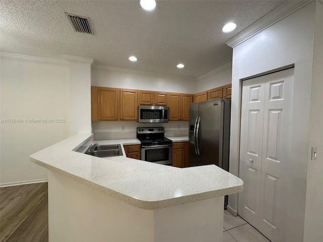 kitchen with kitchen peninsula, a textured ceiling, appliances with stainless steel finishes, and crown molding