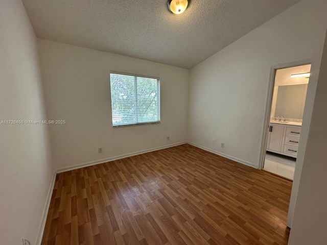 unfurnished bedroom with sink, a textured ceiling, vaulted ceiling, and hardwood / wood-style floors