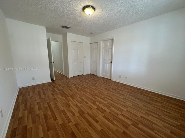 unfurnished bedroom featuring a textured ceiling, dark wood-type flooring, and multiple closets