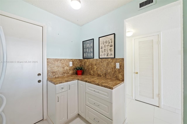 kitchen with a textured ceiling, white cabinetry, light tile patterned flooring, and tasteful backsplash