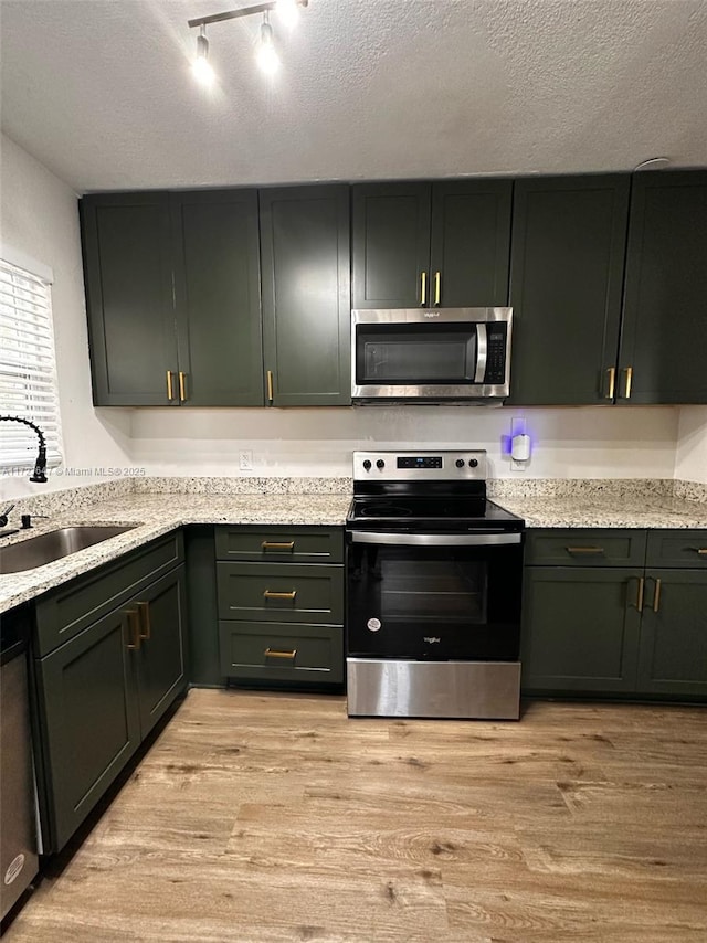 kitchen with appliances with stainless steel finishes, light wood-type flooring, and a textured ceiling