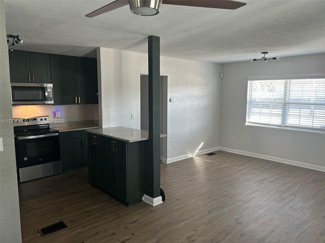 kitchen with dark wood-type flooring, ceiling fan, light stone counters, and appliances with stainless steel finishes