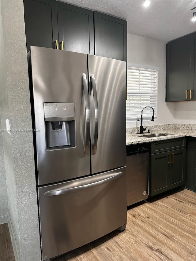 kitchen featuring appliances with stainless steel finishes, light hardwood / wood-style flooring, light stone counters, and sink