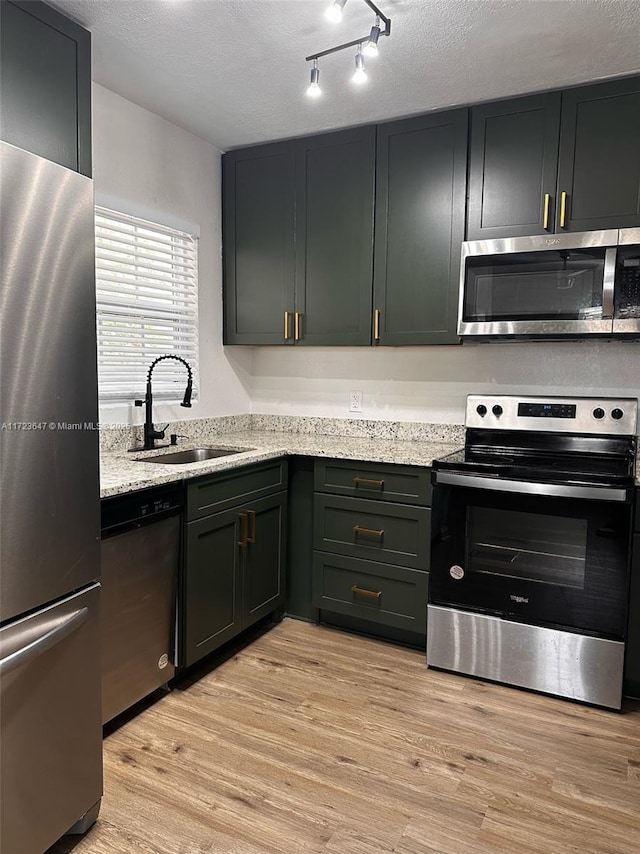 kitchen with light stone counters, a textured ceiling, light wood-type flooring, appliances with stainless steel finishes, and sink