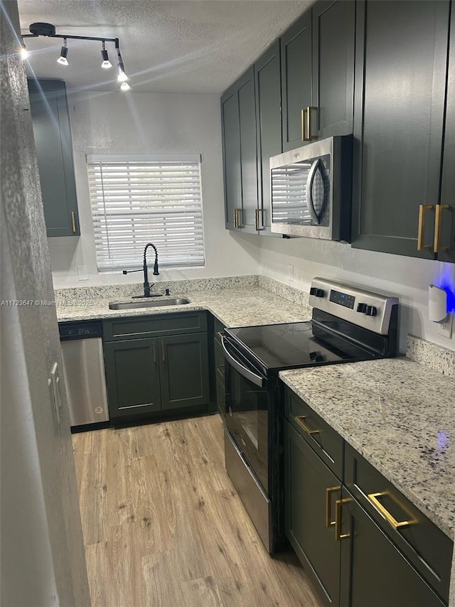 kitchen with appliances with stainless steel finishes, a textured ceiling, light stone counters, sink, and light hardwood / wood-style flooring